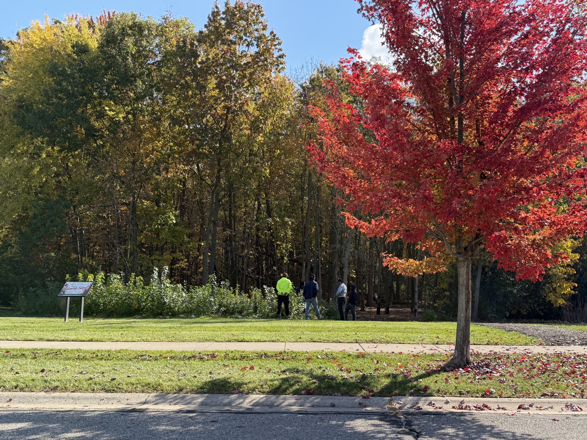 People gathered beside the wooded garden site beneath a brilliant red maple at The Preserve.